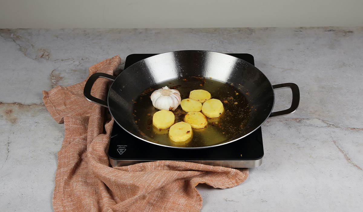 Sofreír patatas y ajo para Arroz al horno en paella