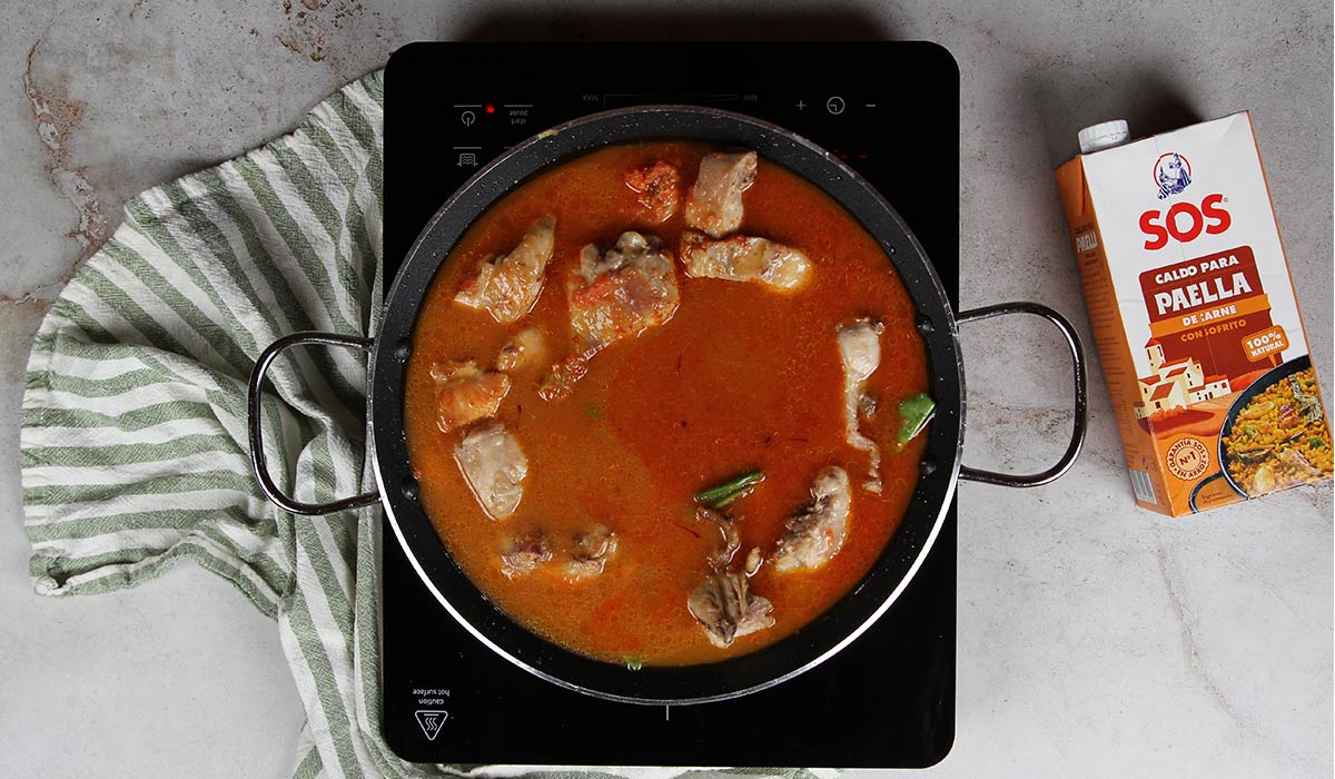 Añadir caldo en Paella con conejo y pollo