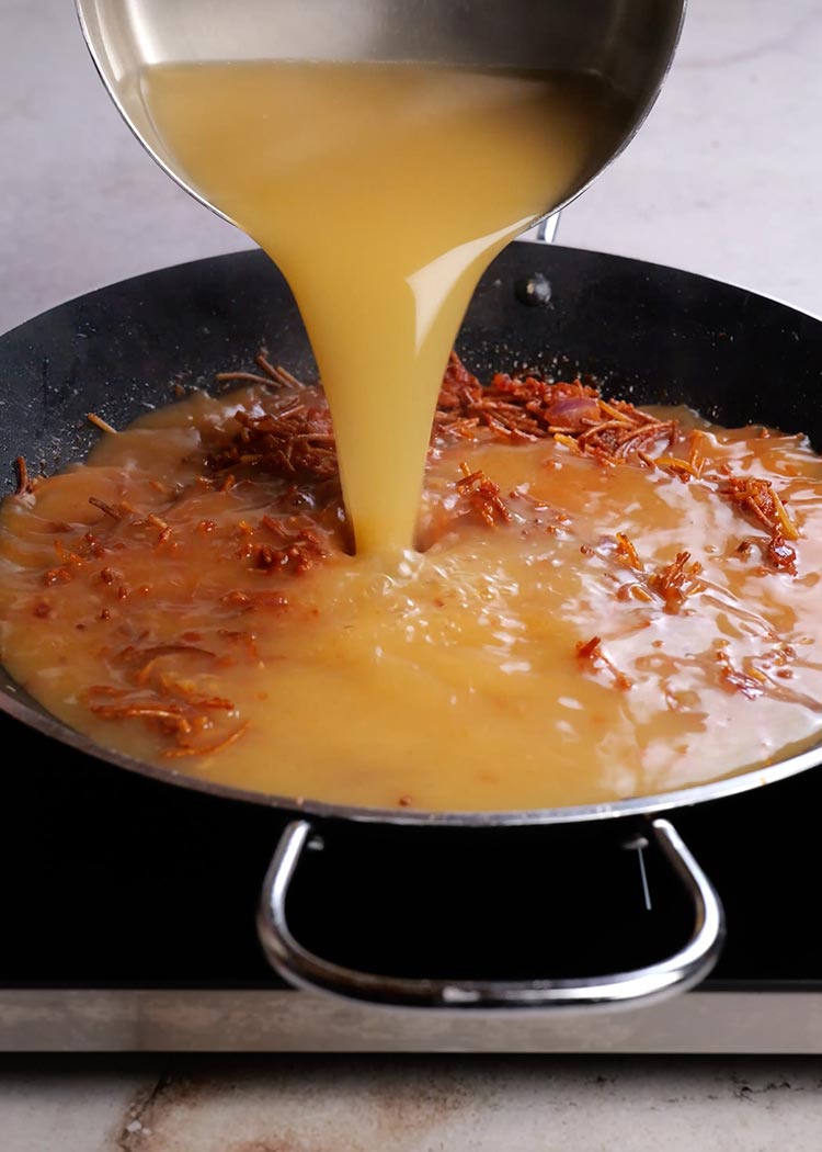 Añadir fideos y caldo a fideua con calamares y gambas 